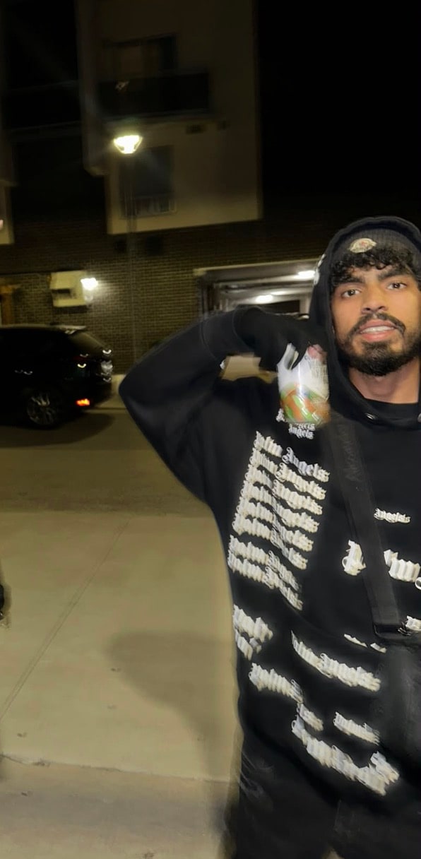 DRTYEIGHT at night in a black Palm Angels hoodie, hood up, mid-shot outside a parking garage